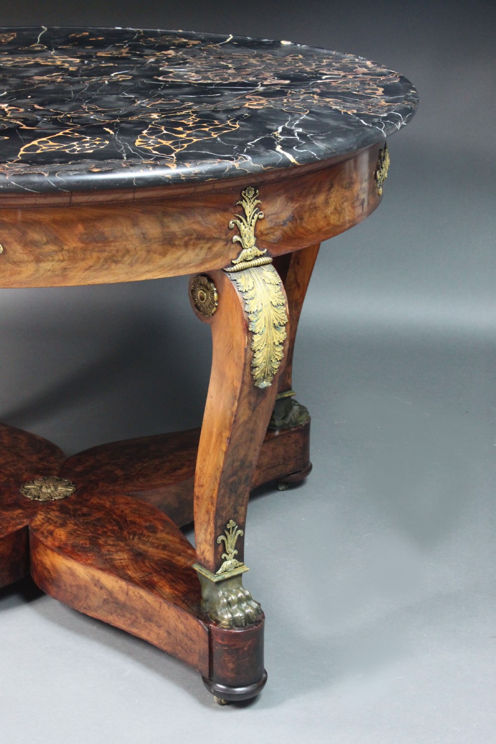 A circular French Empire centre table featuring a black veined marble top, mahogany apron with gilt bronze mounts, and curved legs on a cruciform base. View XI