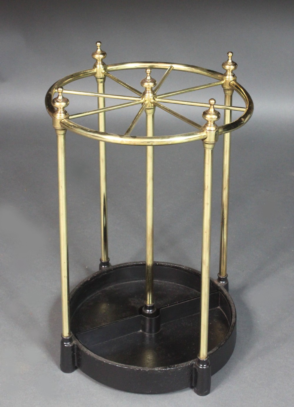 A Victorian circular brass umbrella stand featuring a divided top ring with finials, tubular uprights, and a heavy cast iron drip tray base. View II