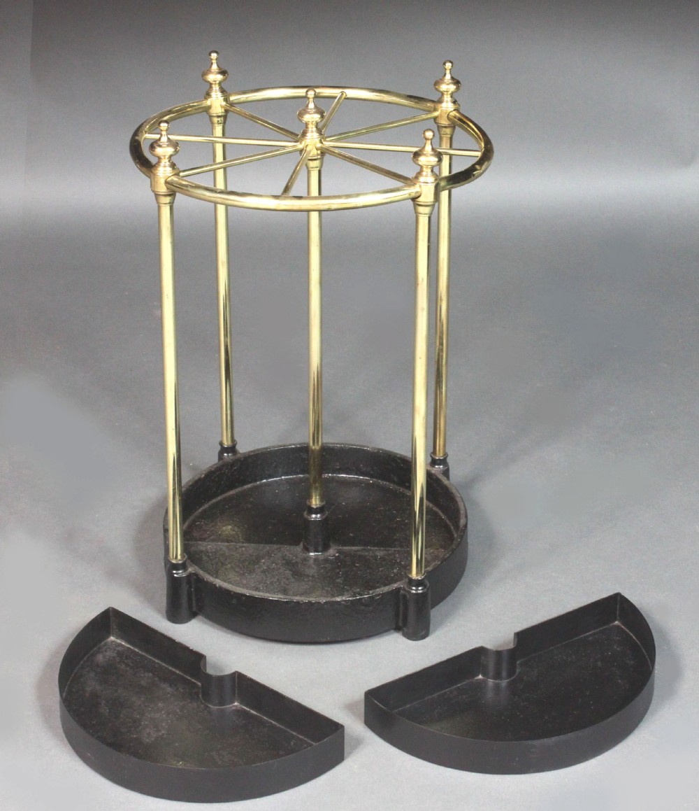 A Victorian circular brass umbrella stand featuring a divided top ring with finials, tubular uprights, and a heavy cast iron drip tray base. View III
