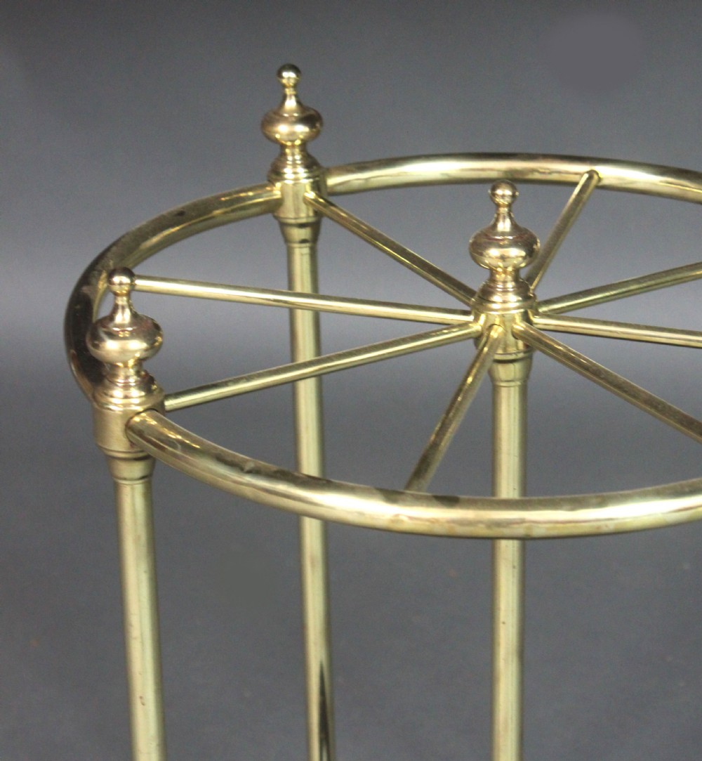 A Victorian circular brass umbrella stand featuring a divided top ring with finials, tubular uprights, and a heavy cast iron drip tray base. View IV