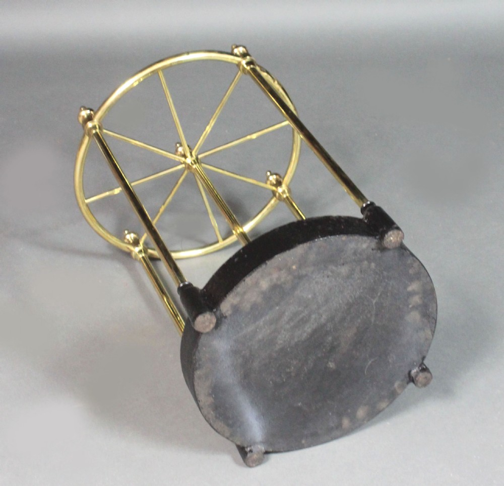 A Victorian circular brass umbrella stand featuring a divided top ring with finials, tubular uprights, and a heavy cast iron drip tray base. View V