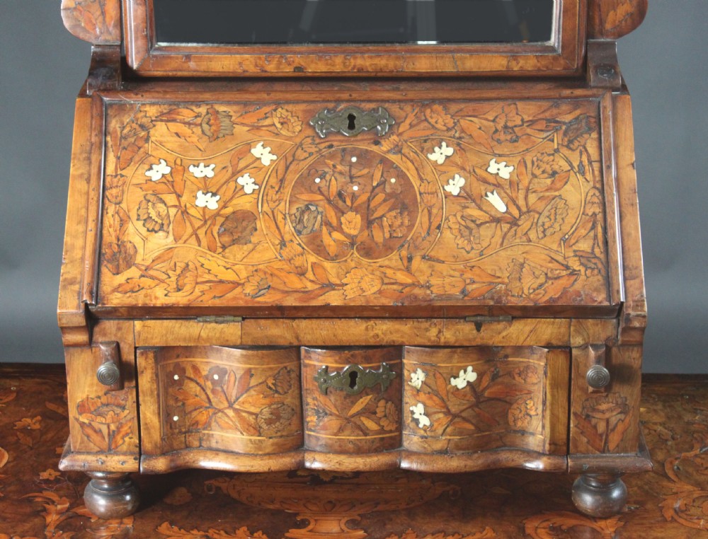 An antique Dutch walnut toilet mirror featuring detailed floral marquetry inlay, an arched frame, and a slant-front drawer base supported by bun feet. View V