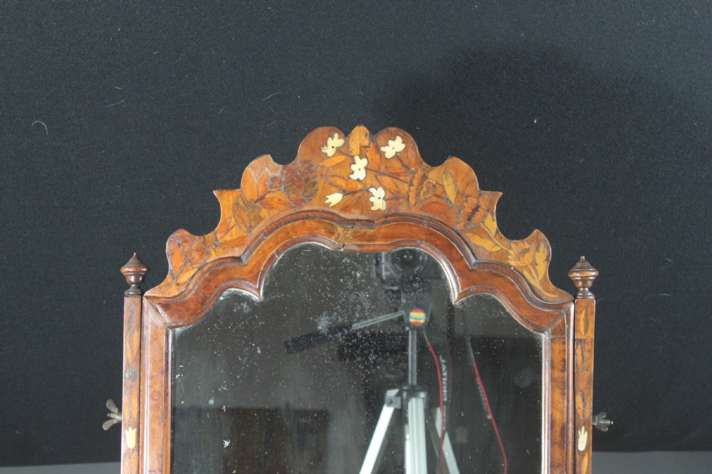 An antique Dutch walnut toilet mirror featuring detailed floral marquetry inlay, an arched frame, and a slant-front drawer base supported by bun feet. View VI