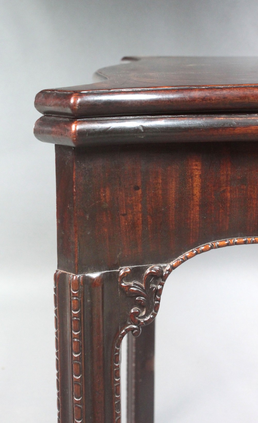 An 18th-century Chippendale style mahogany card table featuring a serpentine fold-over top, carved apron edge, and square moulded legs. View V