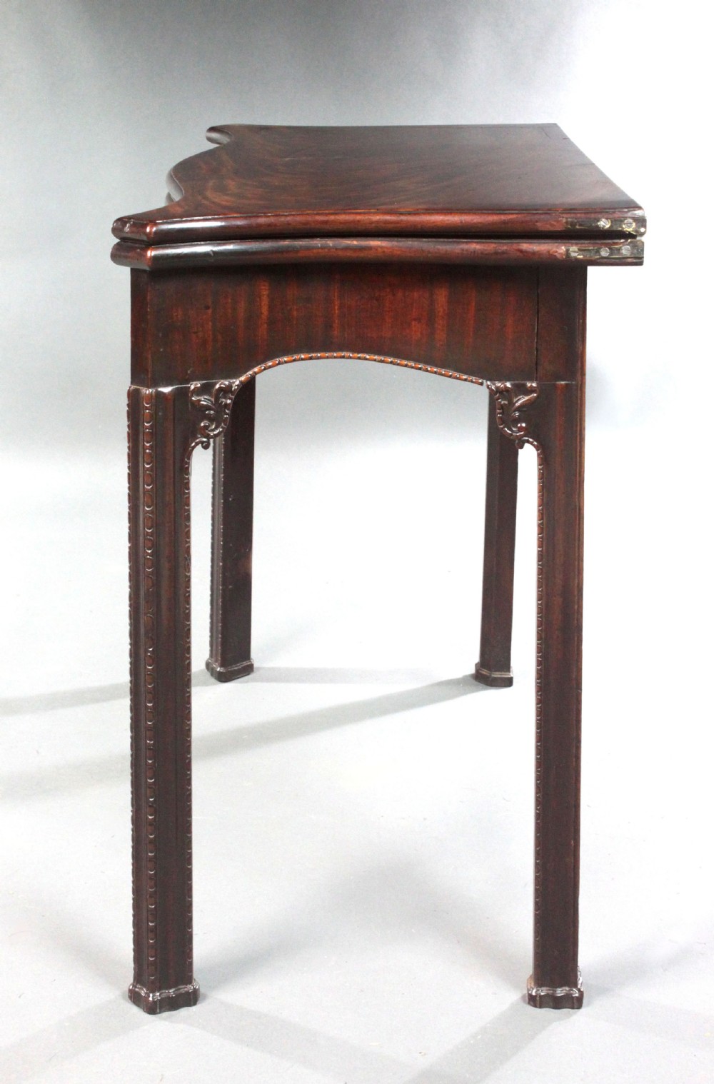 An 18th-century Chippendale style mahogany card table featuring a serpentine fold-over top, carved apron edge, and square moulded legs. View VI