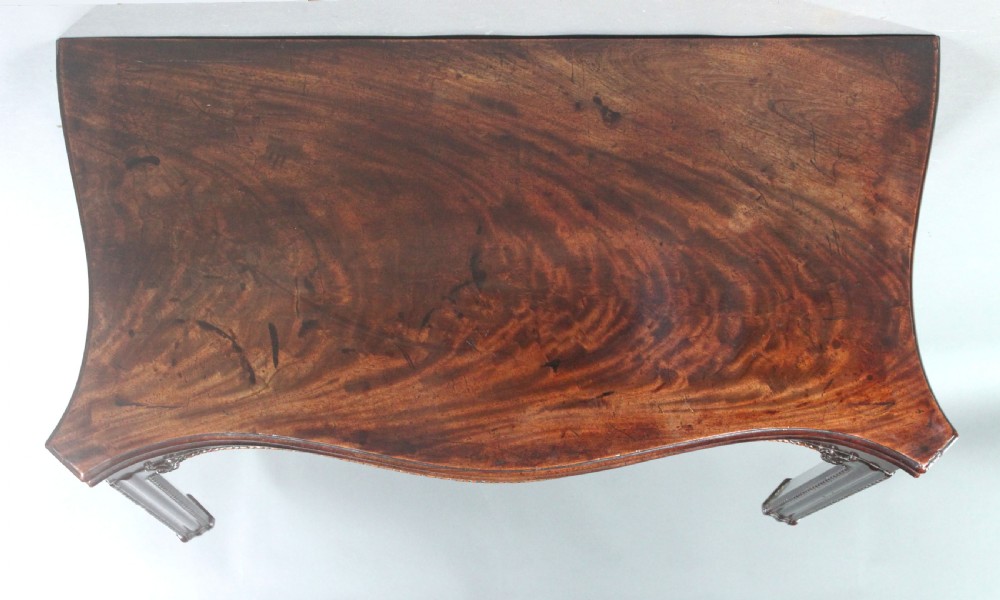 An 18th-century Chippendale style mahogany card table featuring a serpentine fold-over top, carved apron edge, and square moulded legs. View VII