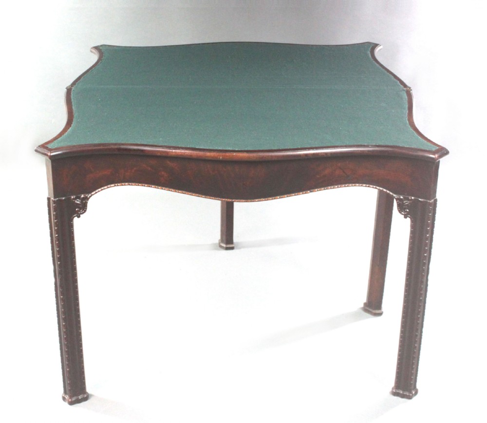 An 18th-century Chippendale style mahogany card table featuring a serpentine fold-over top, carved apron edge, and square moulded legs. View VIII