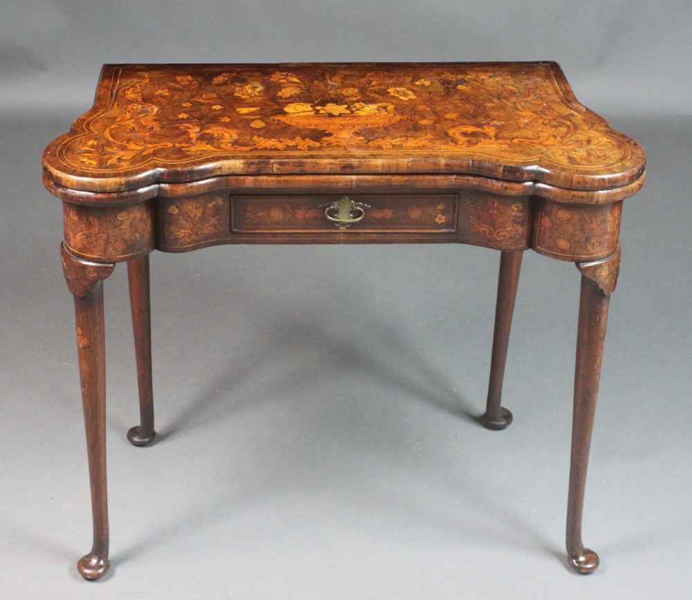 An antique Dutch walnut card table featuring detailed floral marquetry inlay, a serpentine frieze with a single drawer, and slender legs.