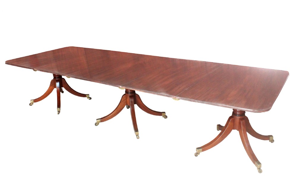 A long Regency mahogany dining table supported by three central pedestal bases with splayed legs and brass castors.