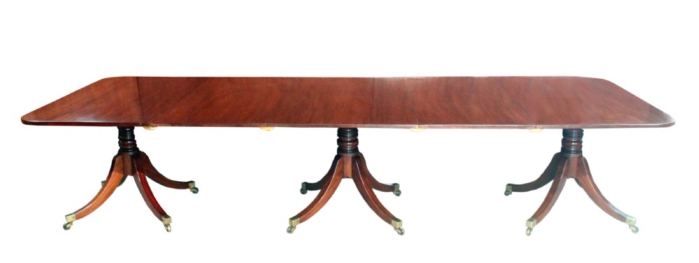 A long Regency mahogany dining table supported by three central pedestal bases with splayed legs and brass castors. View II