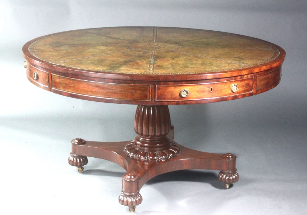 A circular Georgian mahogany drum table featuring a green leather inset top with gilt tooling, frieze drawers with brass handles, and a carved pedestal base resting on four splayed legs with castors. View II