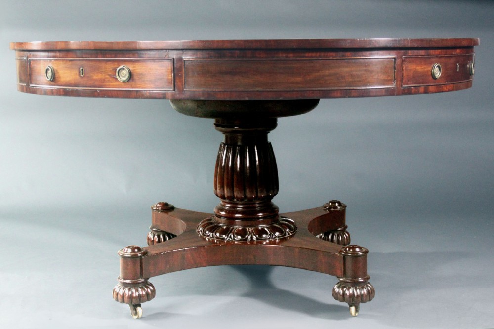 A circular Georgian mahogany drum table featuring a green leather inset top with gilt tooling, frieze drawers with brass handles, and a carved pedestal base resting on four splayed legs with castors. View III
