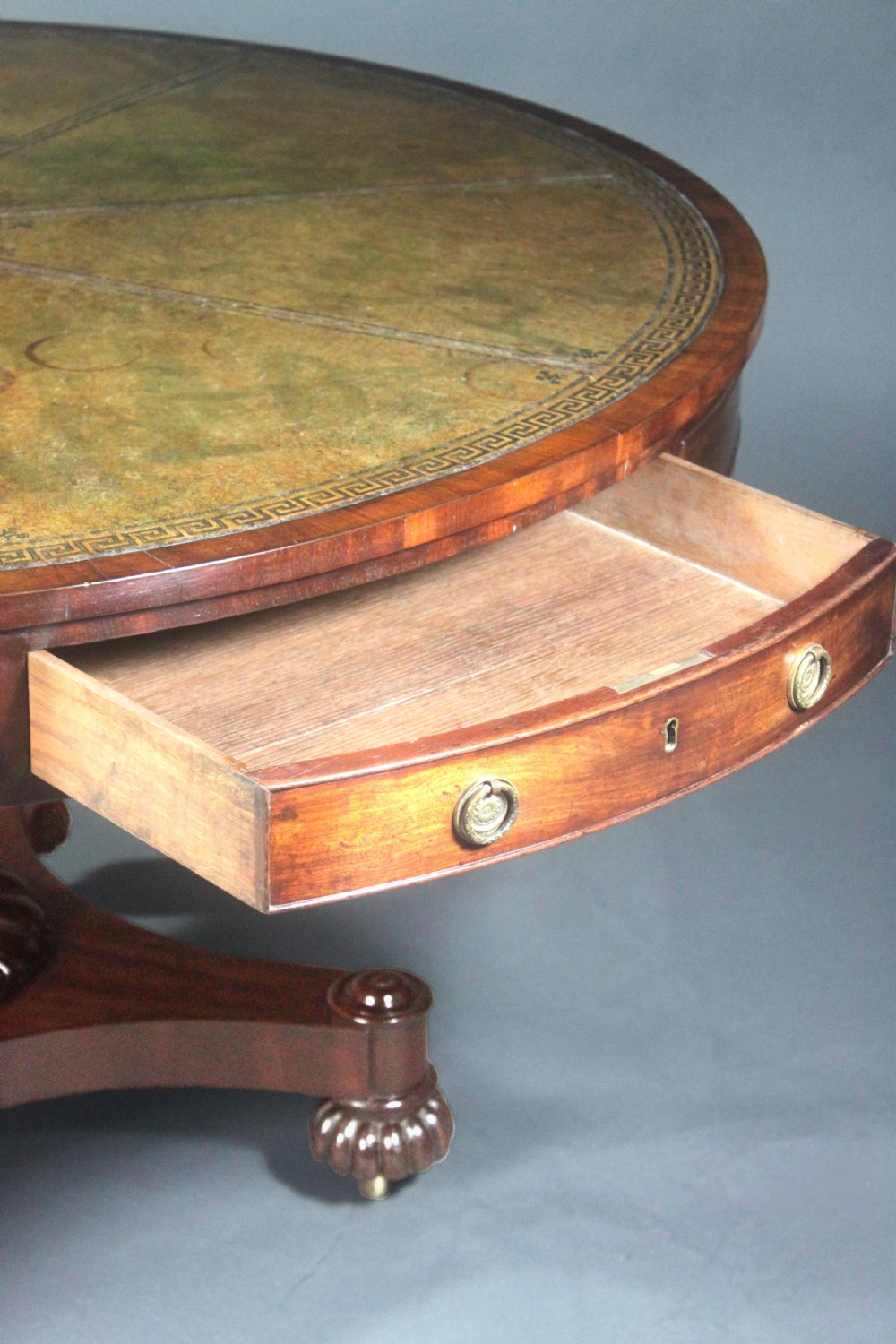 A circular Georgian mahogany drum table featuring a green leather inset top with gilt tooling, frieze drawers with brass handles, and a carved pedestal base resting on four splayed legs with castors. View VII