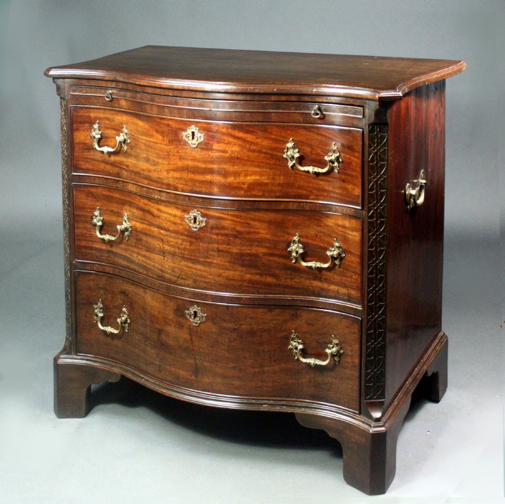 An eighteenth-century George III mahogany chest of drawers featuring a serpentine front, carved blind fretwork, brass handles, and bracket feet.
