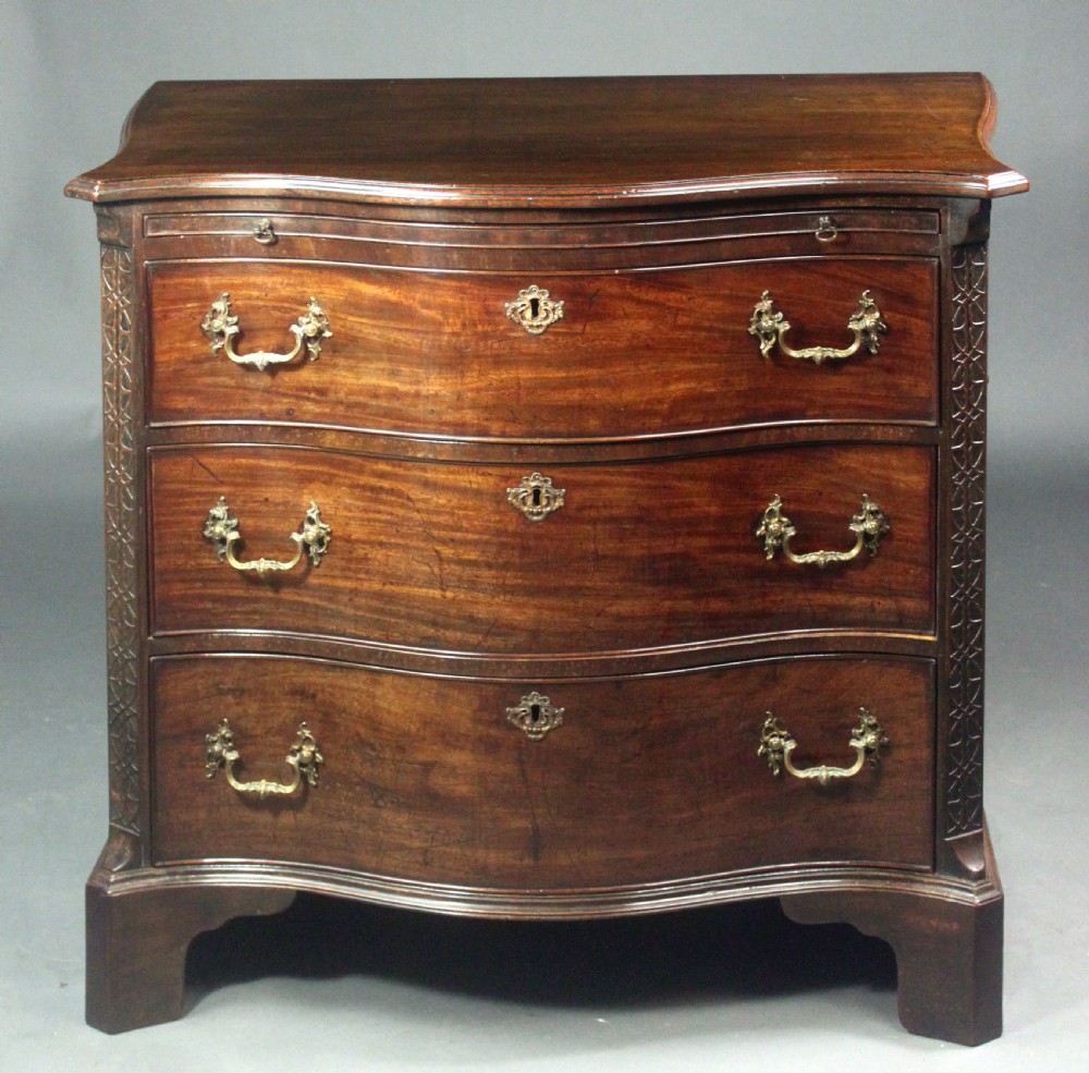 An eighteenth-century George III mahogany chest of drawers featuring a serpentine front, carved blind fretwork, brass handles, and bracket feet. View II