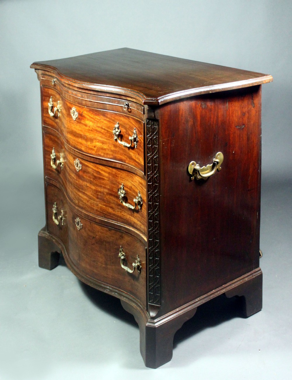 An eighteenth-century George III mahogany chest of drawers featuring a serpentine front, carved blind fretwork, brass handles, and bracket feet. View III