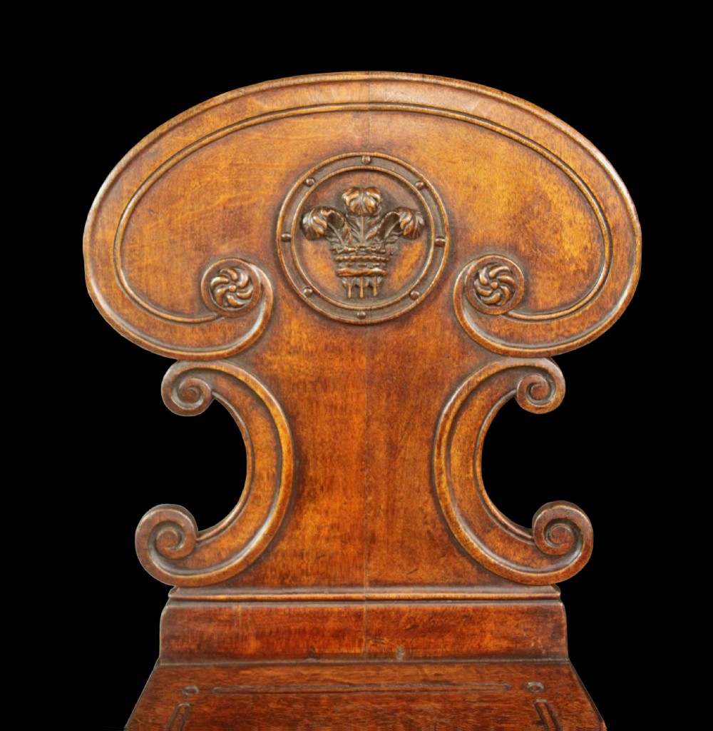 A pair of Regency oak hall chairs featuring shaped scroll backrests with central carved medallions, solid seats, and turned fluted front legs. View II