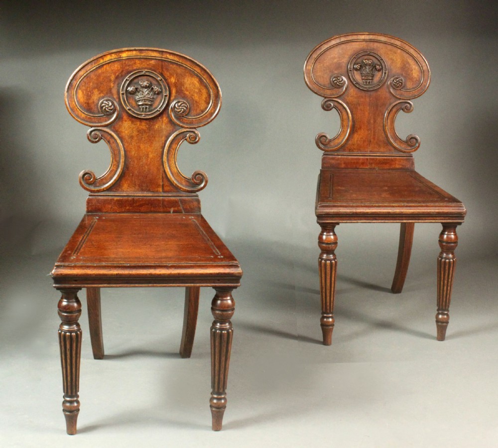 A pair of Regency oak hall chairs featuring shaped scroll backrests with central carved medallions, solid seats, and turned fluted front legs. View III