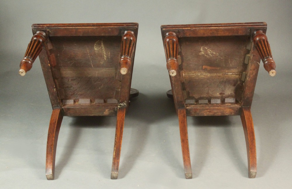 A pair of Regency oak hall chairs featuring shaped scroll backrests with central carved medallions, solid seats, and turned fluted front legs. View VII