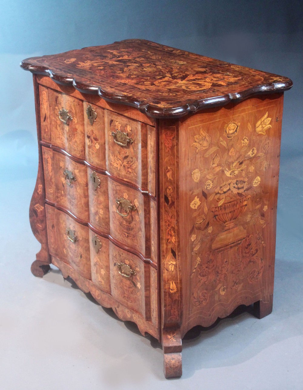 An antique Dutch marquetry chest of drawers featuring three drawers, floral wood inlay, shaped sides, and brass drop handles. View III
