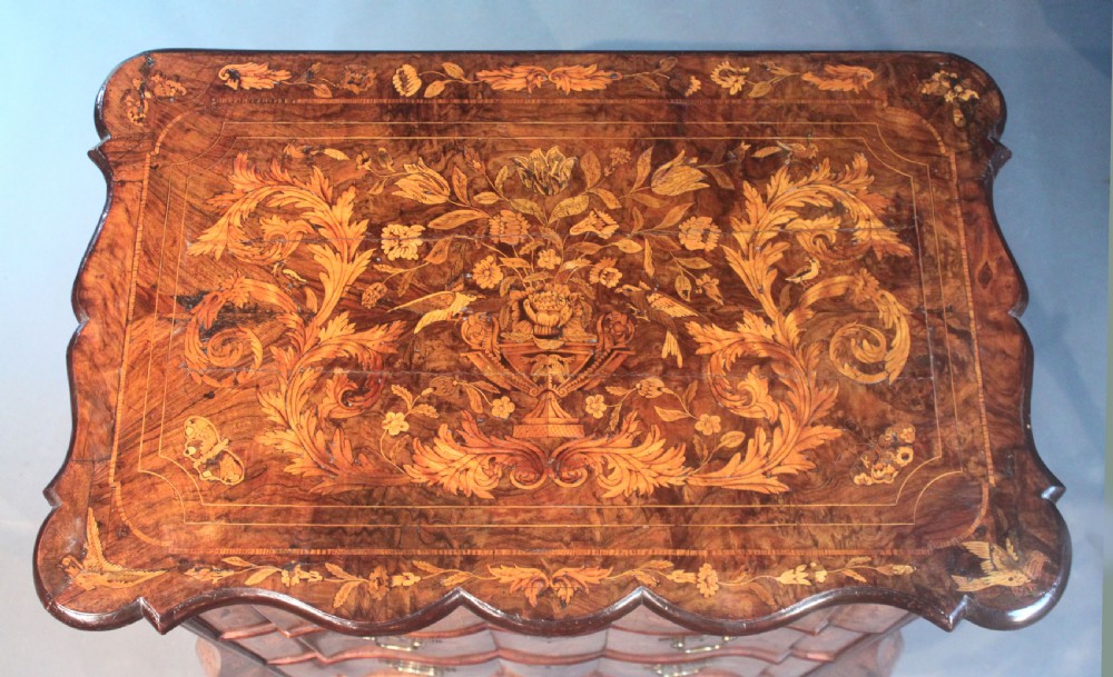 An antique Dutch marquetry chest of drawers featuring three drawers, floral wood inlay, shaped sides, and brass drop handles. View V