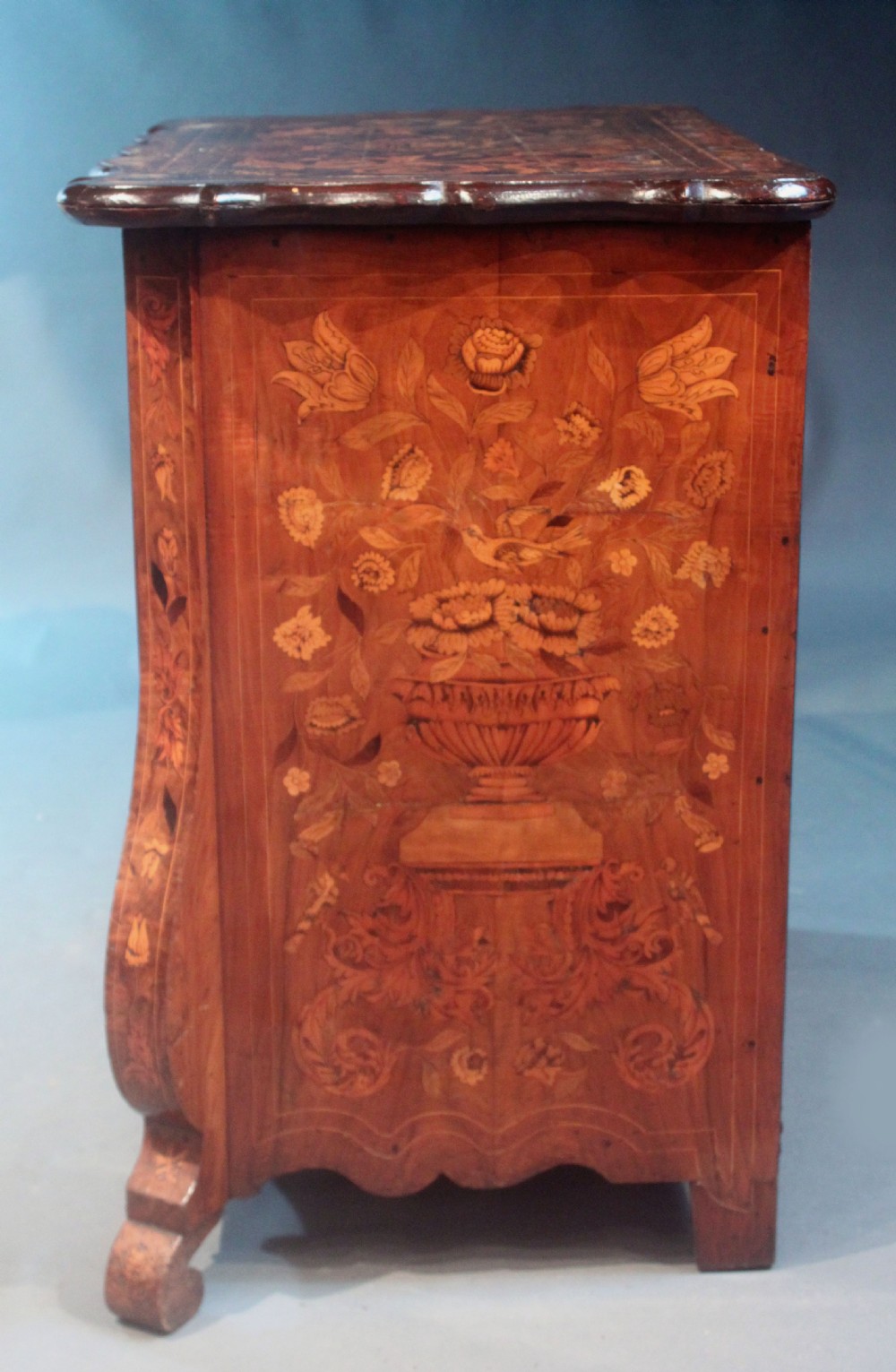 An antique Dutch marquetry chest of drawers featuring three drawers, floral wood inlay, shaped sides, and brass drop handles. View VII