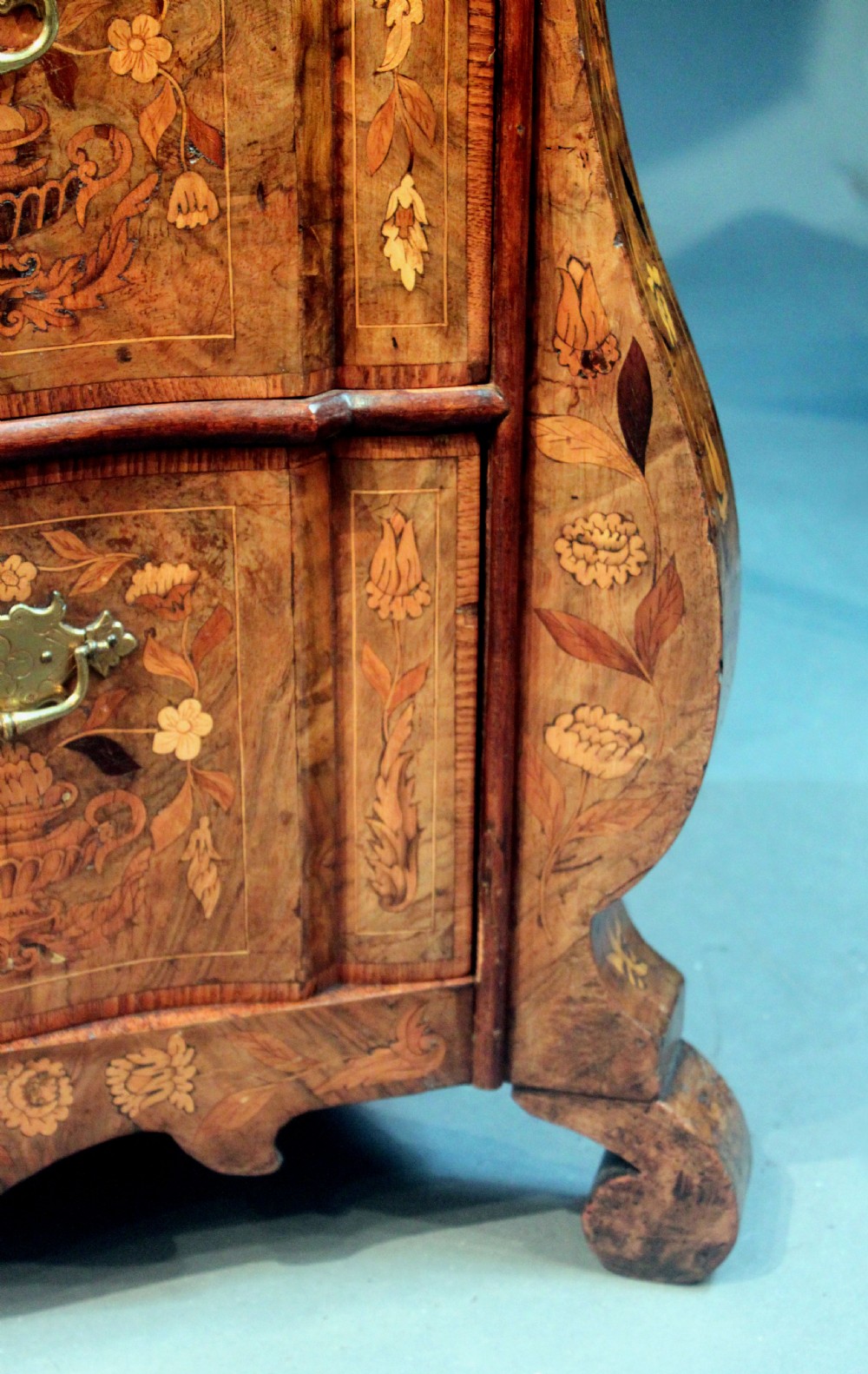 An antique Dutch marquetry chest of drawers featuring three drawers, floral wood inlay, shaped sides, and brass drop handles. View X