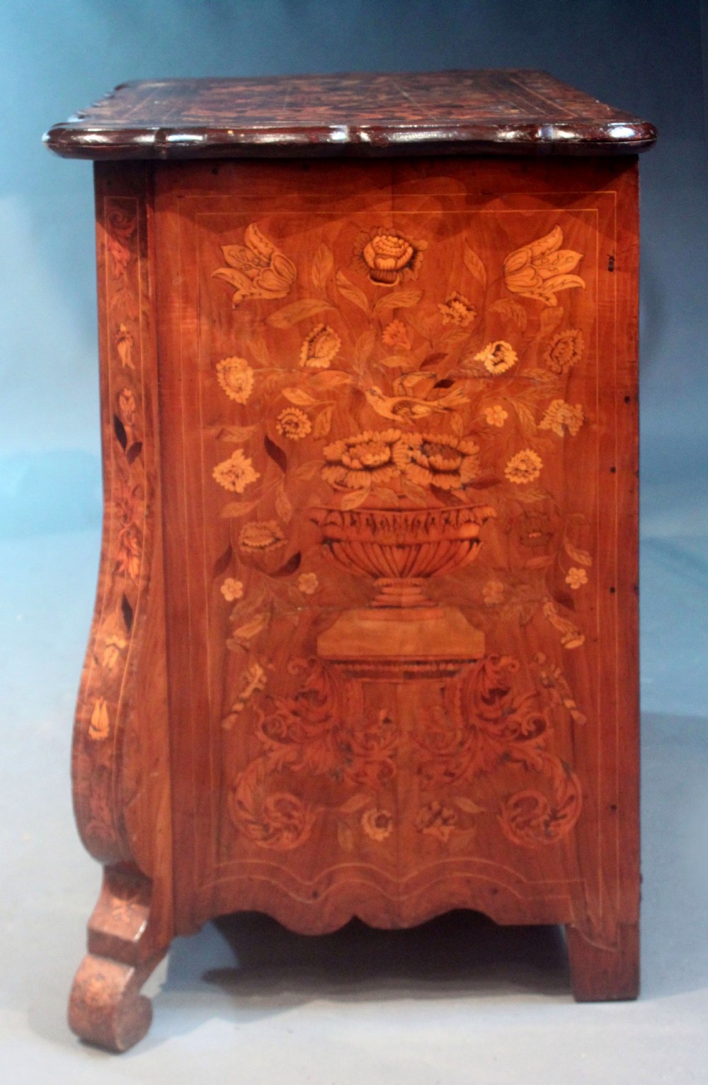 An antique Dutch marquetry chest of drawers featuring three drawers, floral wood inlay, shaped sides, and brass drop handles. View XIII