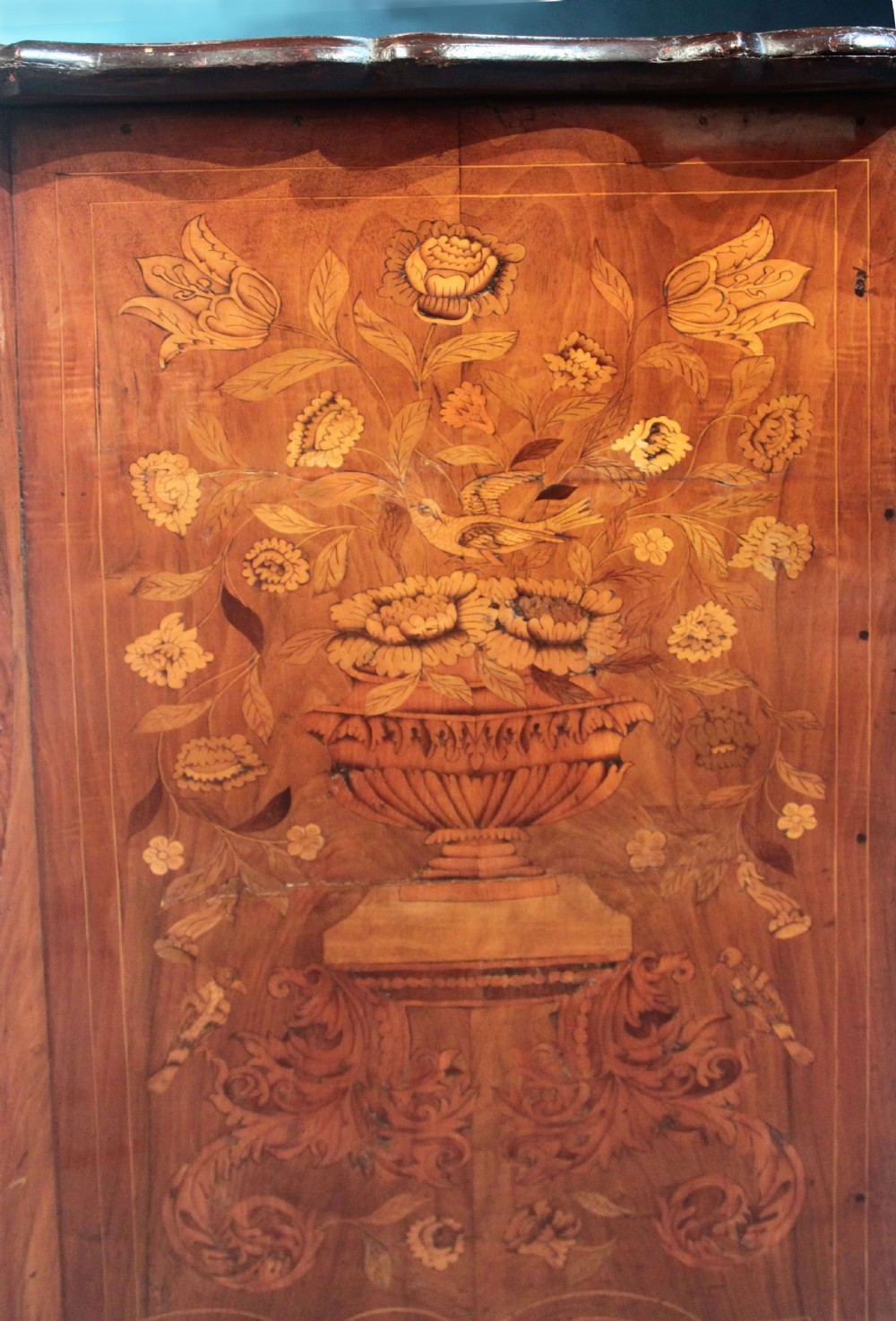 An antique Dutch marquetry chest of drawers featuring three drawers, floral wood inlay, shaped sides, and brass drop handles. View XIV