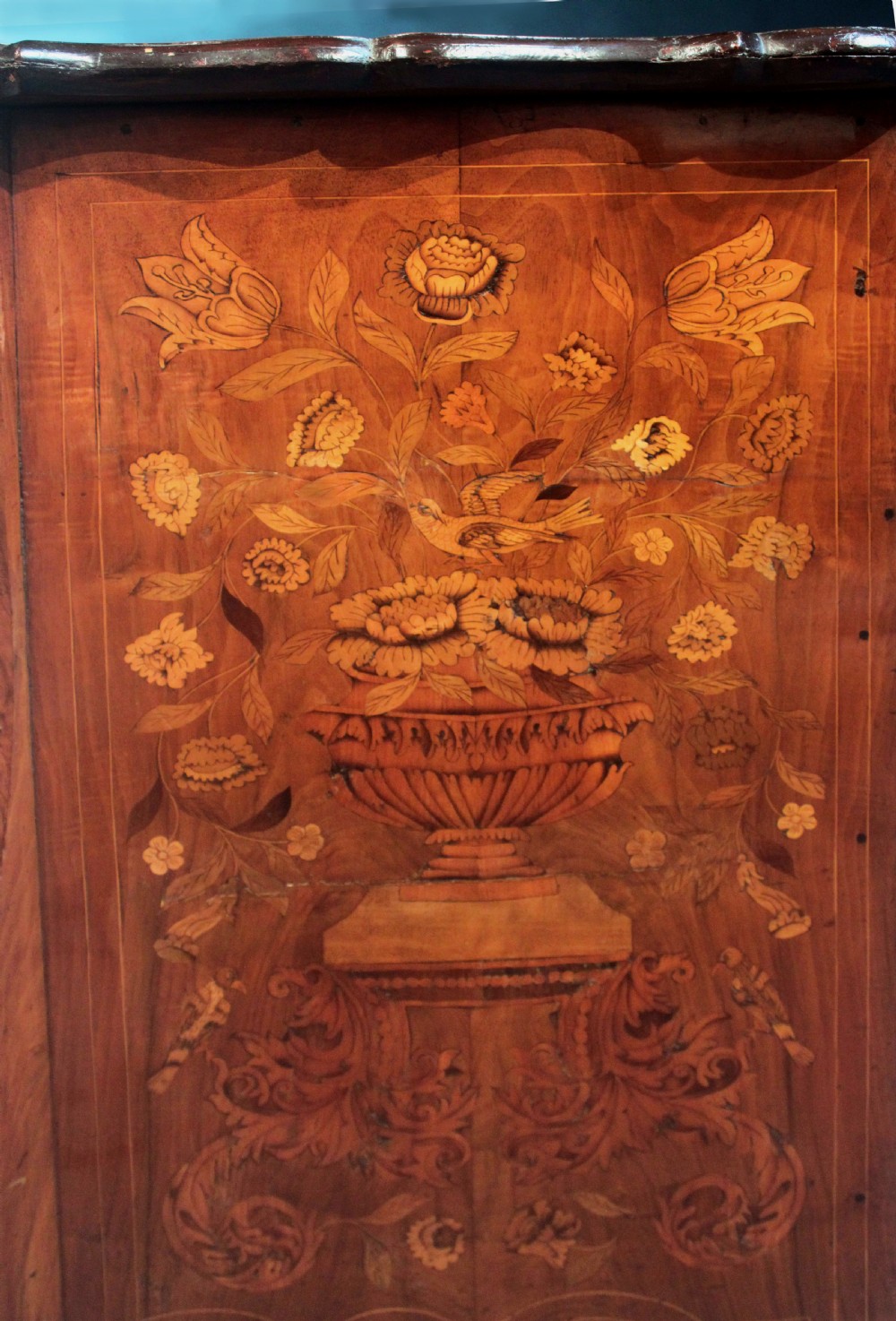 An antique Dutch marquetry chest of drawers featuring three drawers, floral wood inlay, shaped sides, and brass drop handles. View XVII