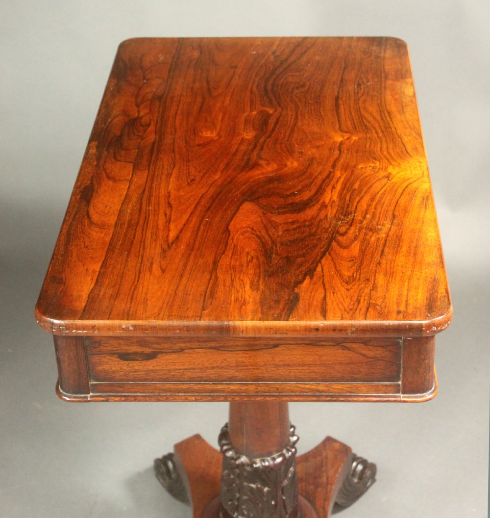 A Regency rosewood occasional table featuring a rectangular top, a tapered carved column support, and a quadform base on scroll feet. View VI