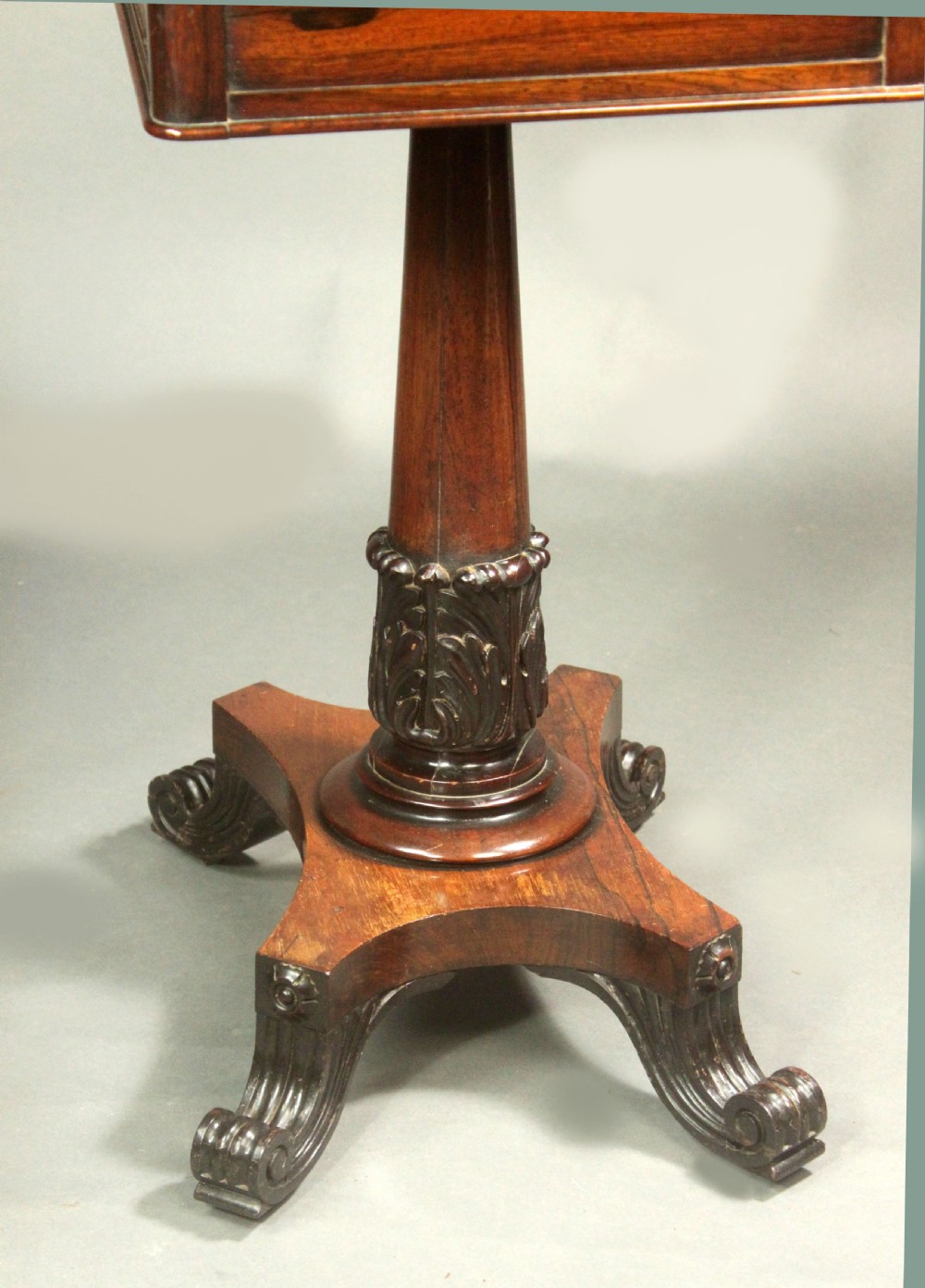 A Regency rosewood occasional table featuring a rectangular top, a tapered carved column support, and a quadform base on scroll feet. View VIII