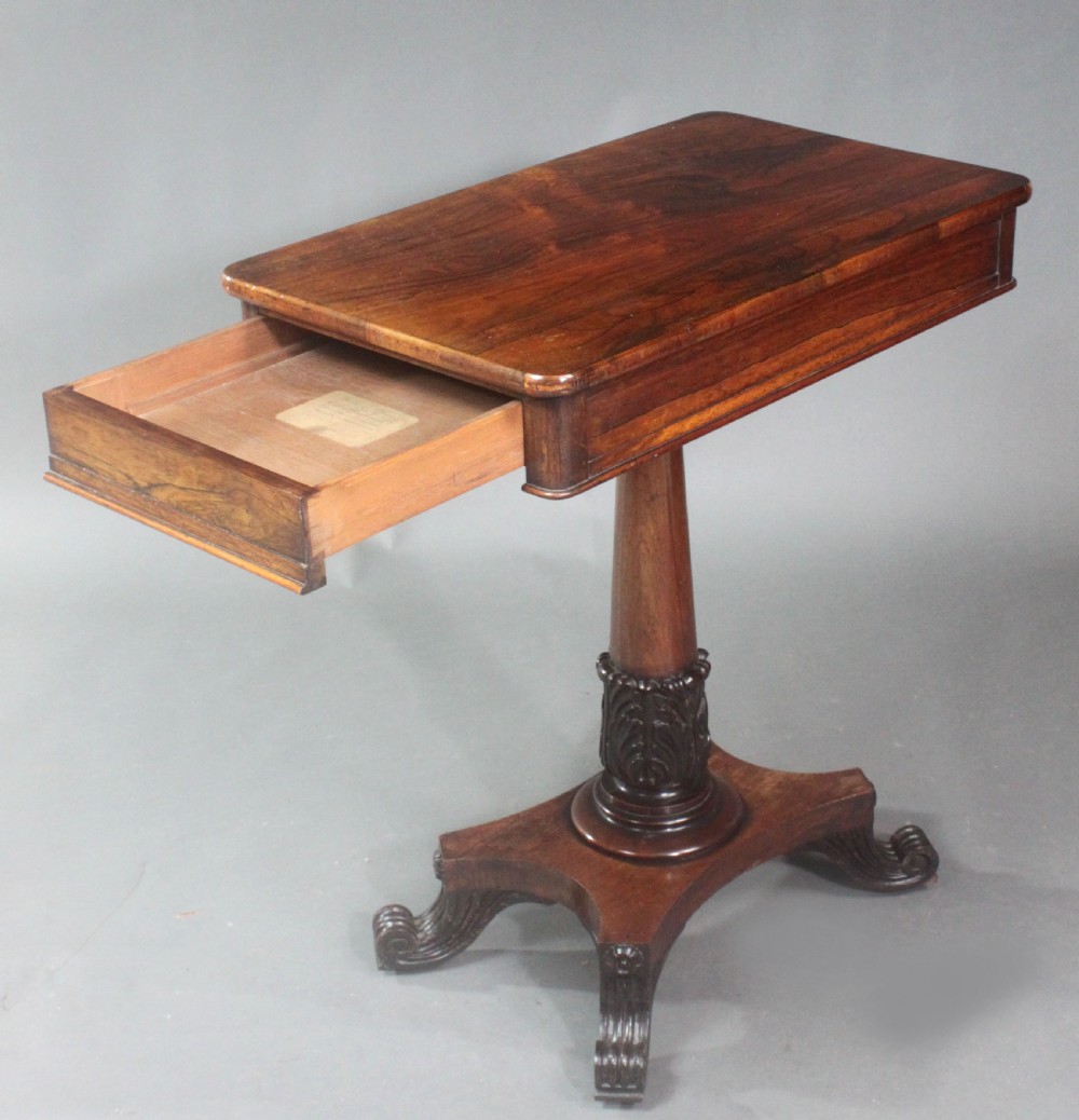 A Regency rosewood occasional table featuring a rectangular top, a tapered carved column support, and a quadform base on scroll feet. View IX
