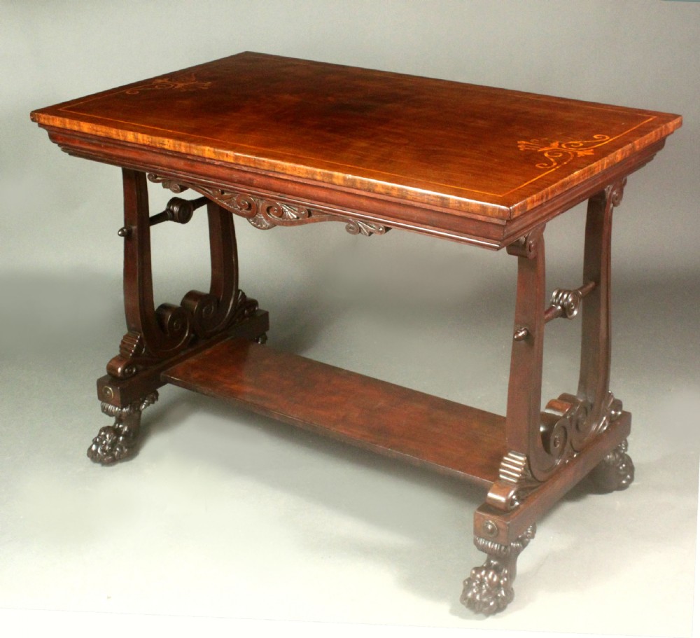 A rectangular Regency mahogany centre table featuring corner inlay, carved scroll supports, a lower stretcher shelf, and carved lion paw feet.