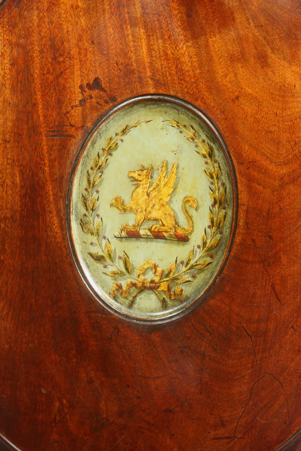 A pair of George III mahogany hall chairs featuring oval backrests with central painted armorial crests, solid timber seats, and square tapered legs. View V