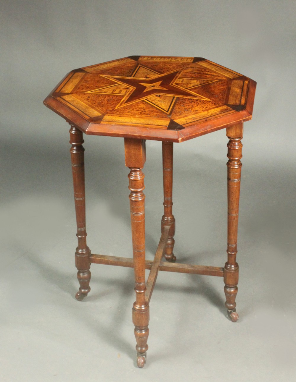An octagonal side table featuring a central inlaid star pattern in contrasting timber veneers, set on turned legs with a cross-stretcher and castors.
