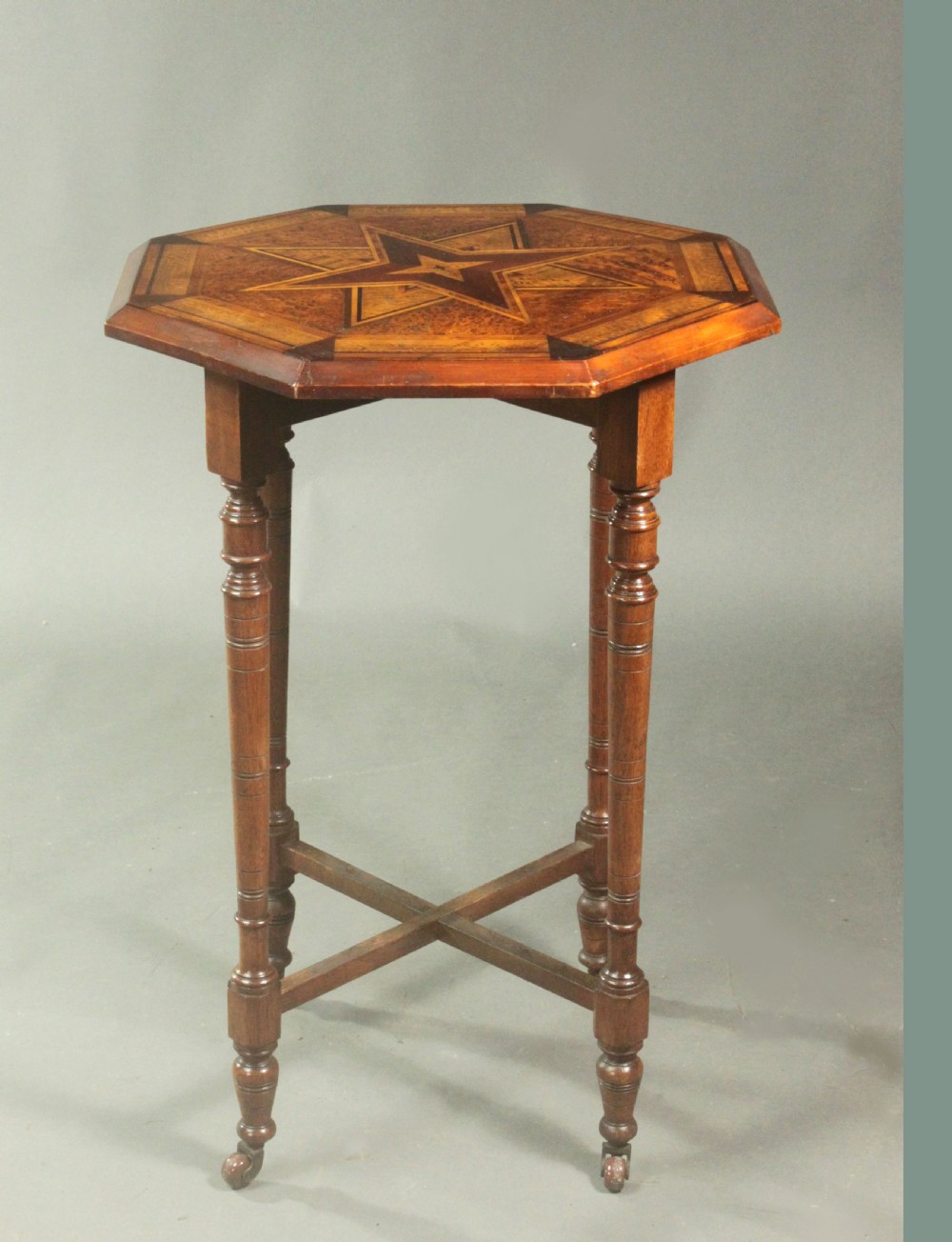 An octagonal side table featuring a central inlaid star pattern in contrasting timber veneers, set on turned legs with a cross-stretcher and castors. View III