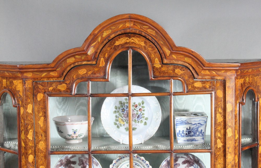 An antique Dutch marquetry glazed cabinet featuring intricate floral wood inlays, glazed doors, an arched pediment, and shaped legs with a stretcher base. View III