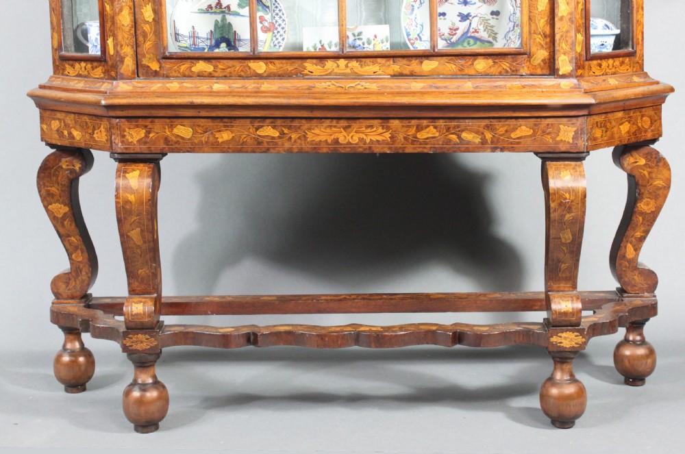 An antique Dutch marquetry glazed cabinet featuring intricate floral wood inlays, glazed doors, an arched pediment, and shaped legs with a stretcher base. View IV