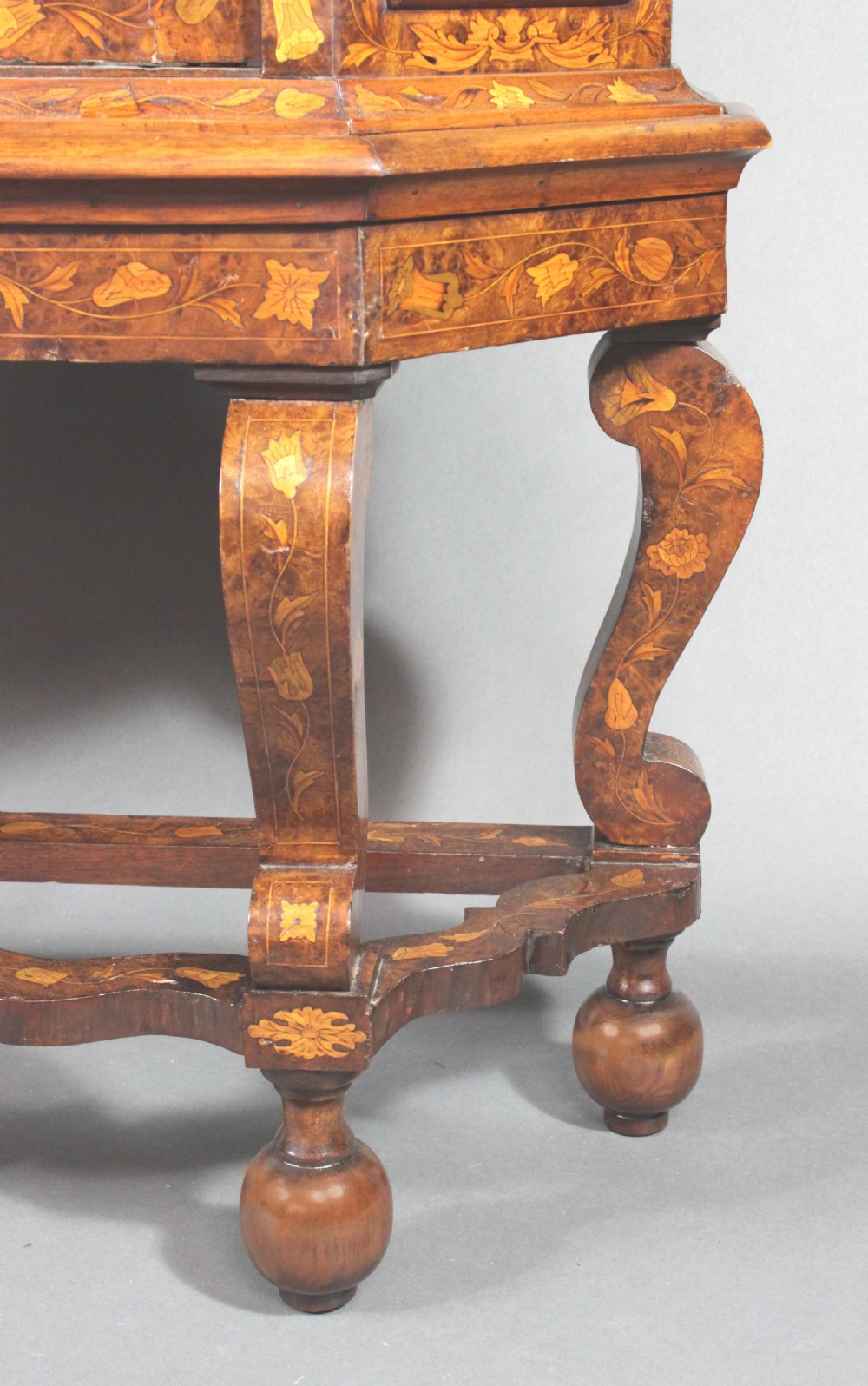 An antique Dutch marquetry glazed cabinet featuring intricate floral wood inlays, glazed doors, an arched pediment, and shaped legs with a stretcher base. View V