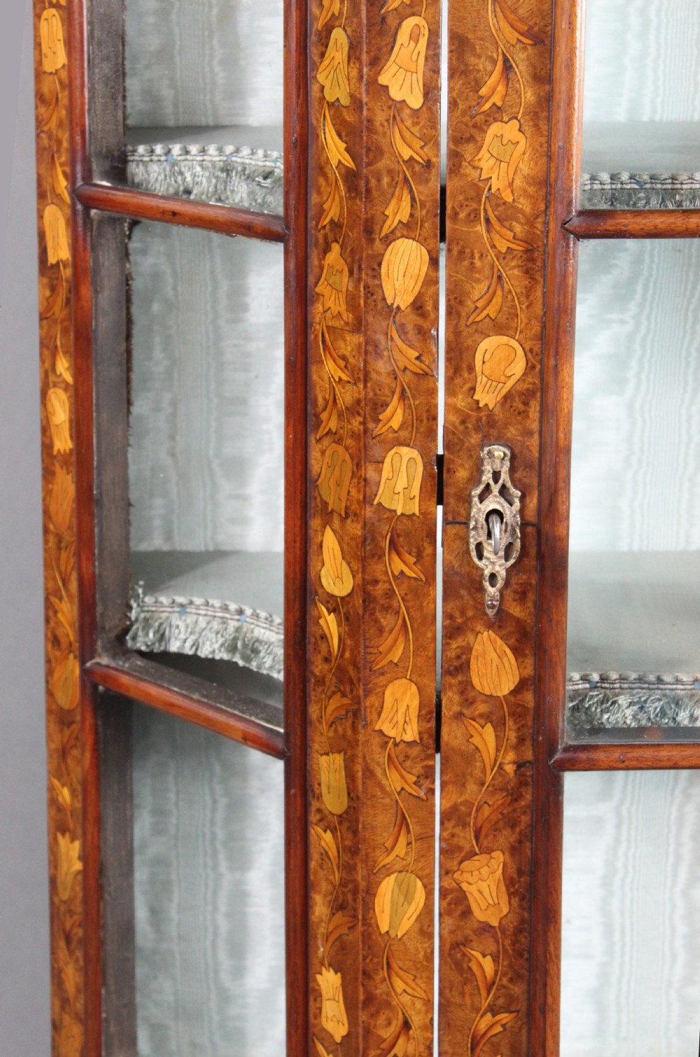 An antique Dutch marquetry glazed cabinet featuring intricate floral wood inlays, glazed doors, an arched pediment, and shaped legs with a stretcher base. View VII