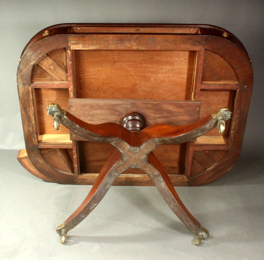 A Regency mahogany centre table featuring a rounded rectangular top, crossbanded border, drawer frieze with brass ring handles, and a reeded quadruped pedestal base with brass lion paw feet on castors. View XIII