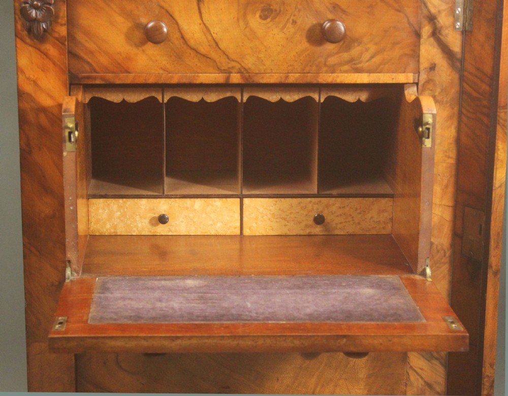 A tall Victorian walnut Wellington chest featuring seven graduated drawers with turned wooden knobs, carved upper corbels, and a right-hand hinged locking flap. View VI