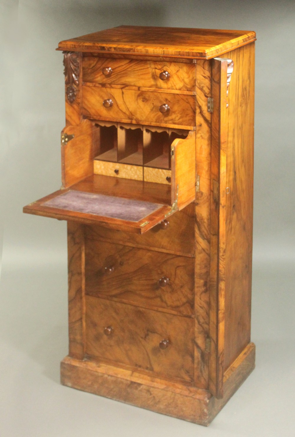 A tall Victorian walnut Wellington chest featuring seven graduated drawers with turned wooden knobs, carved upper corbels, and a right-hand hinged locking flap. View IX