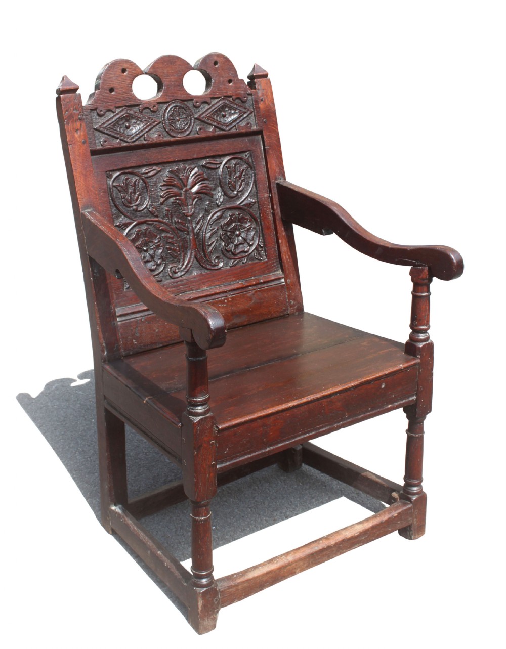 A dark oak wainscot armchair featuring a carved botanical back panel, turned front legs, flat wooden seat, and a crest rail with carved geometric details. View II