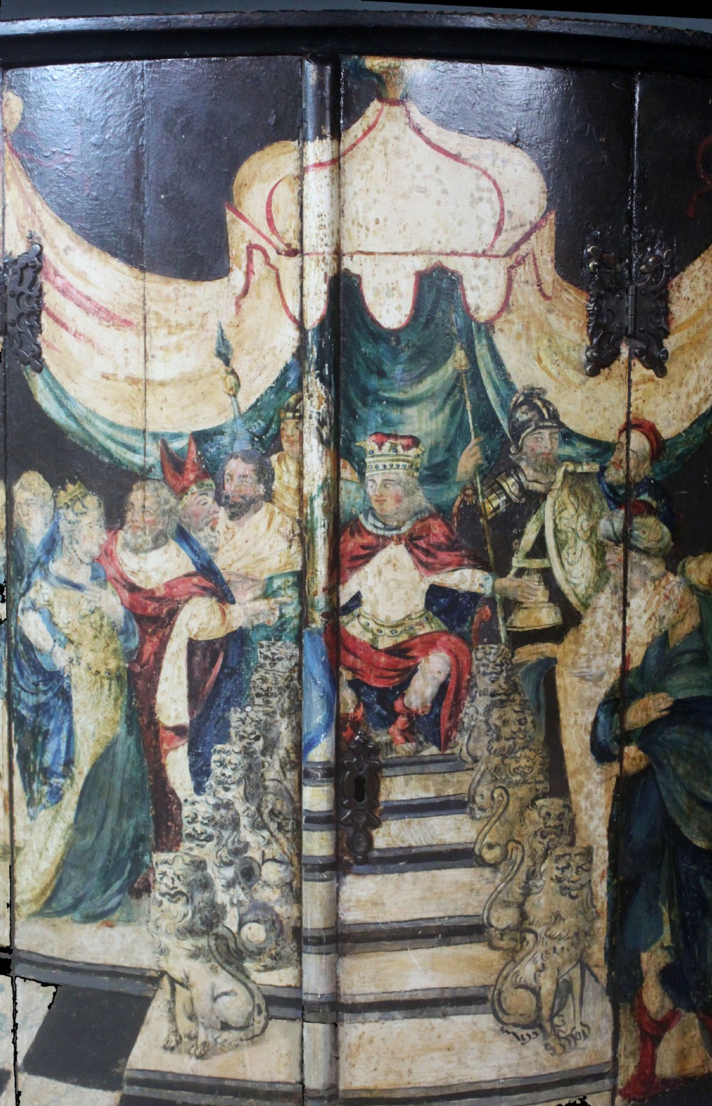 An antique painted hanging corner cupboard featuring a detailed figurative scene with a crowned monarch, courtiers, drapery, and a chequerboard floor across its two doors. View II