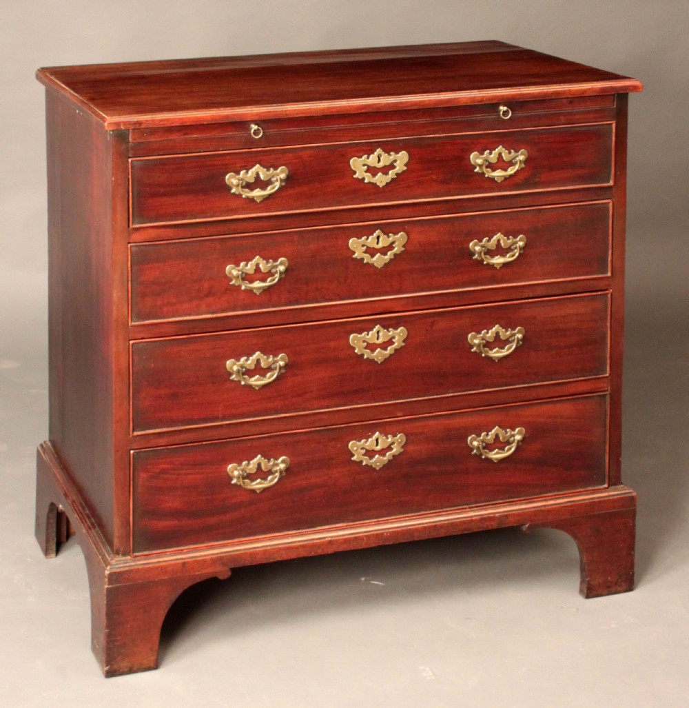 A Georgian mahogany chest featuring four graduated drawers, brass batwing escutcheons and handles, a brushing slide, and bracket feet. View V