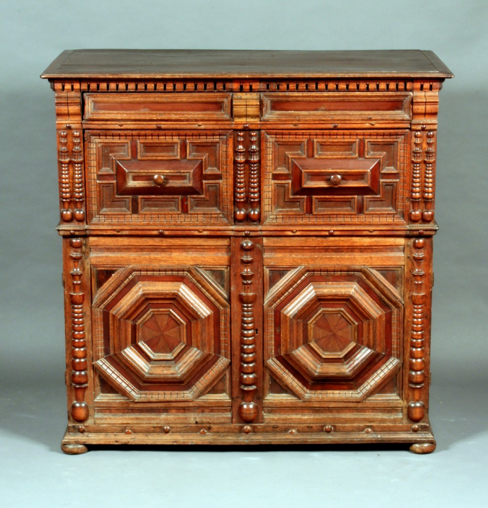 A 17th-century style dark oak chest featuring deep geometric moulded drawers, octagonal lower panel doors, and applied turned split balusters.