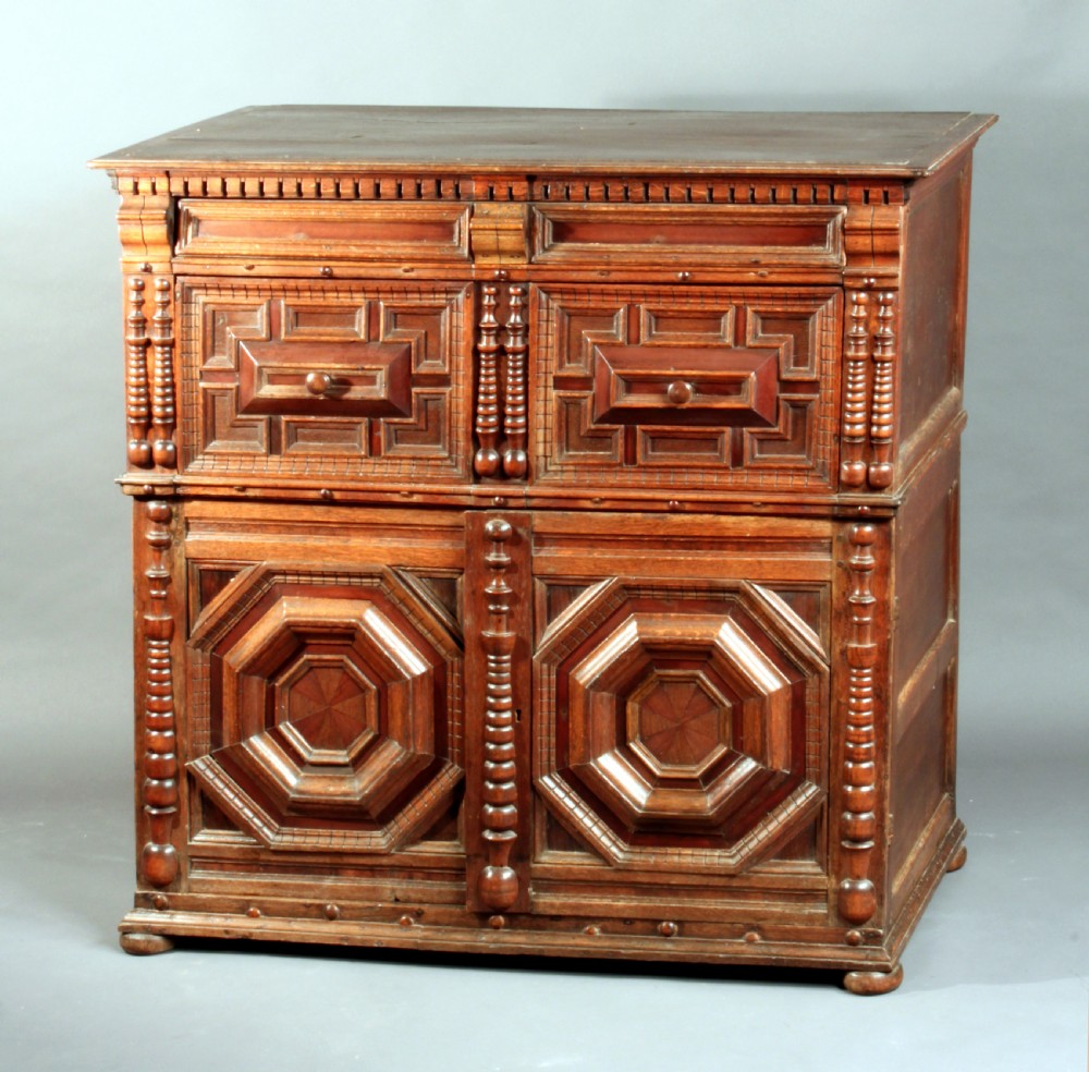 A 17th-century style dark oak chest featuring deep geometric moulded drawers, octagonal lower panel doors, and applied turned split balusters. View II