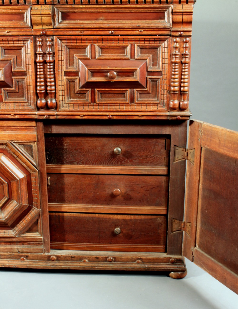 A 17th-century style dark oak chest featuring deep geometric moulded drawers, octagonal lower panel doors, and applied turned split balusters. View III